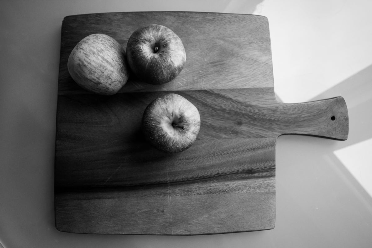 grayscale photo of apple fruit on wooden chopping board