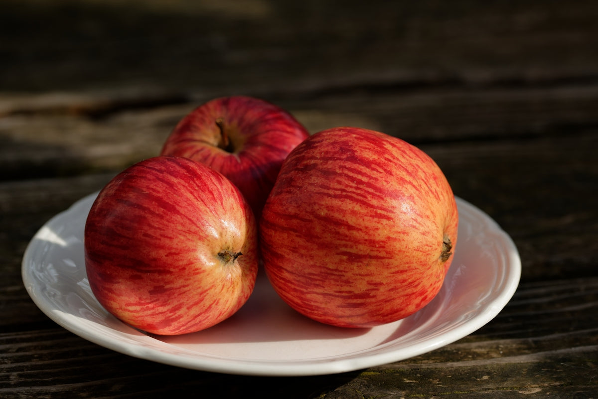 a white plate topped with three red apples