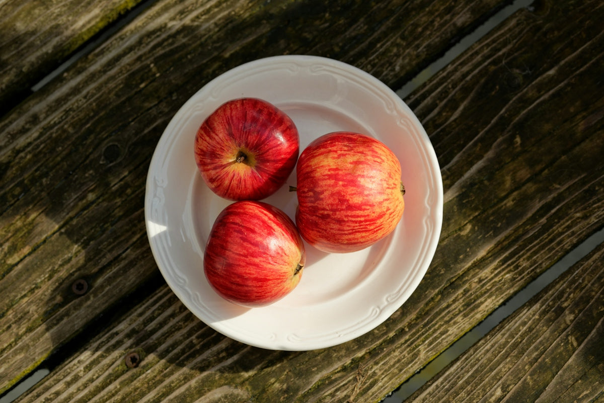 three red apples on a white plate on a wooden table