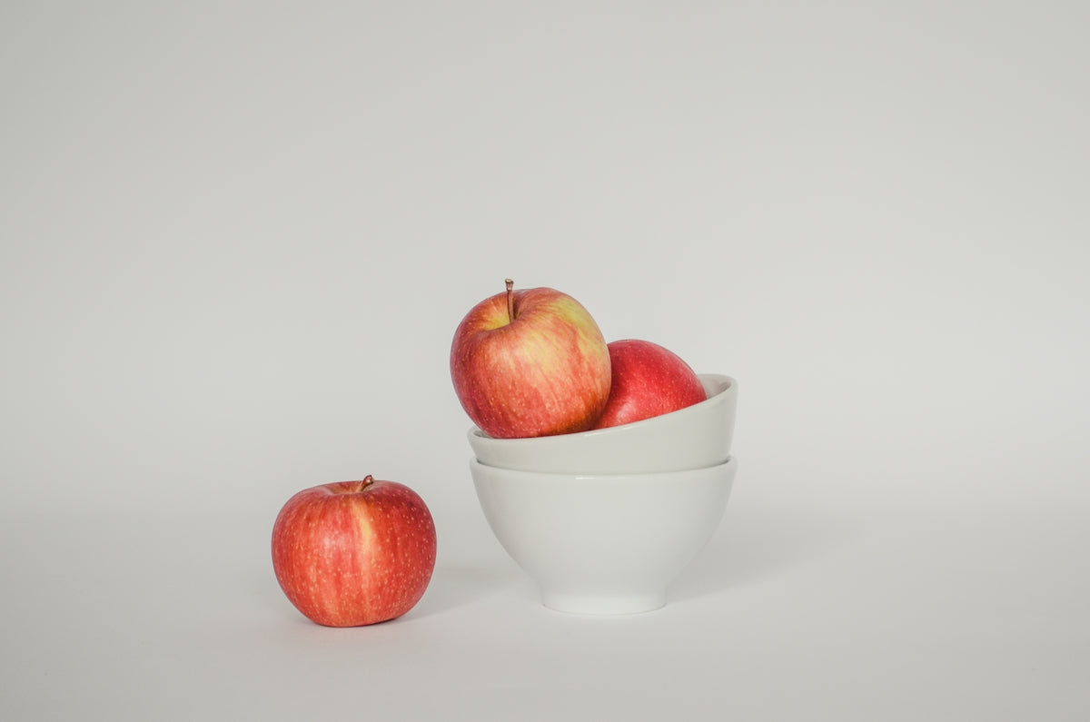 a white bowl filled with red apples on top of a white table