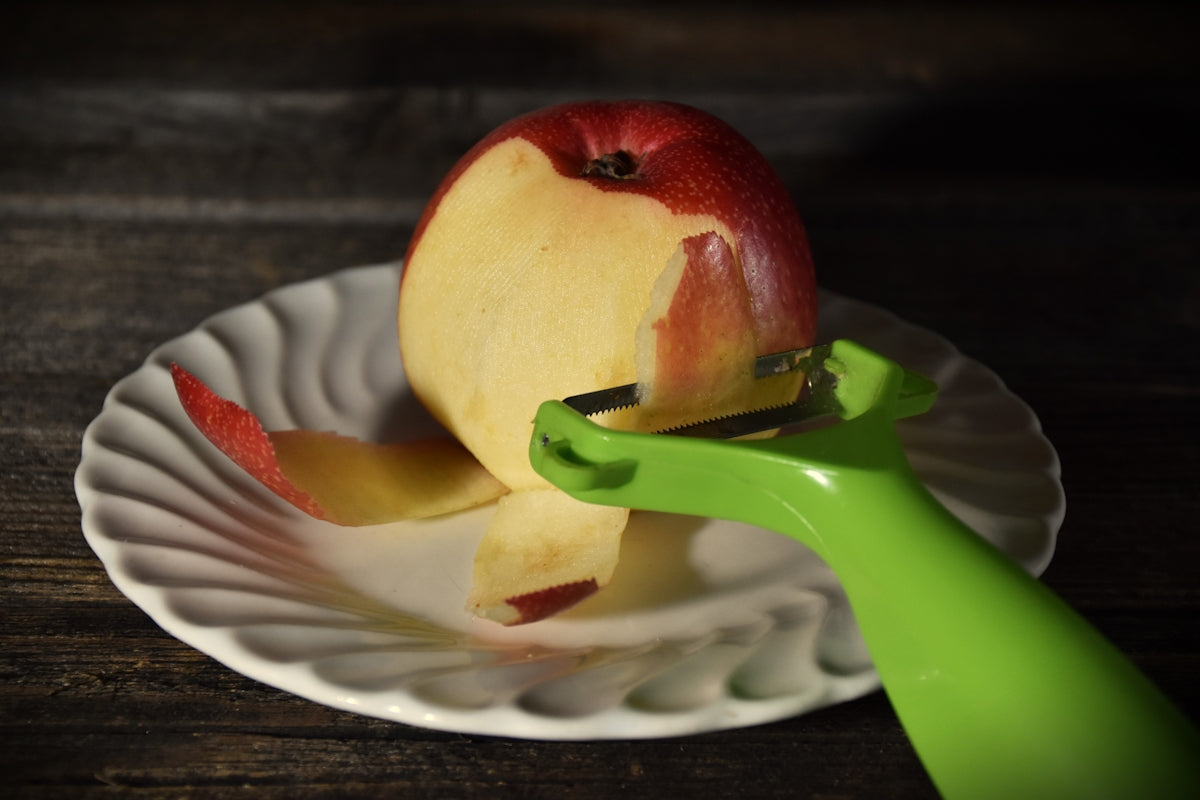 A red apple being peeled on a white plate.